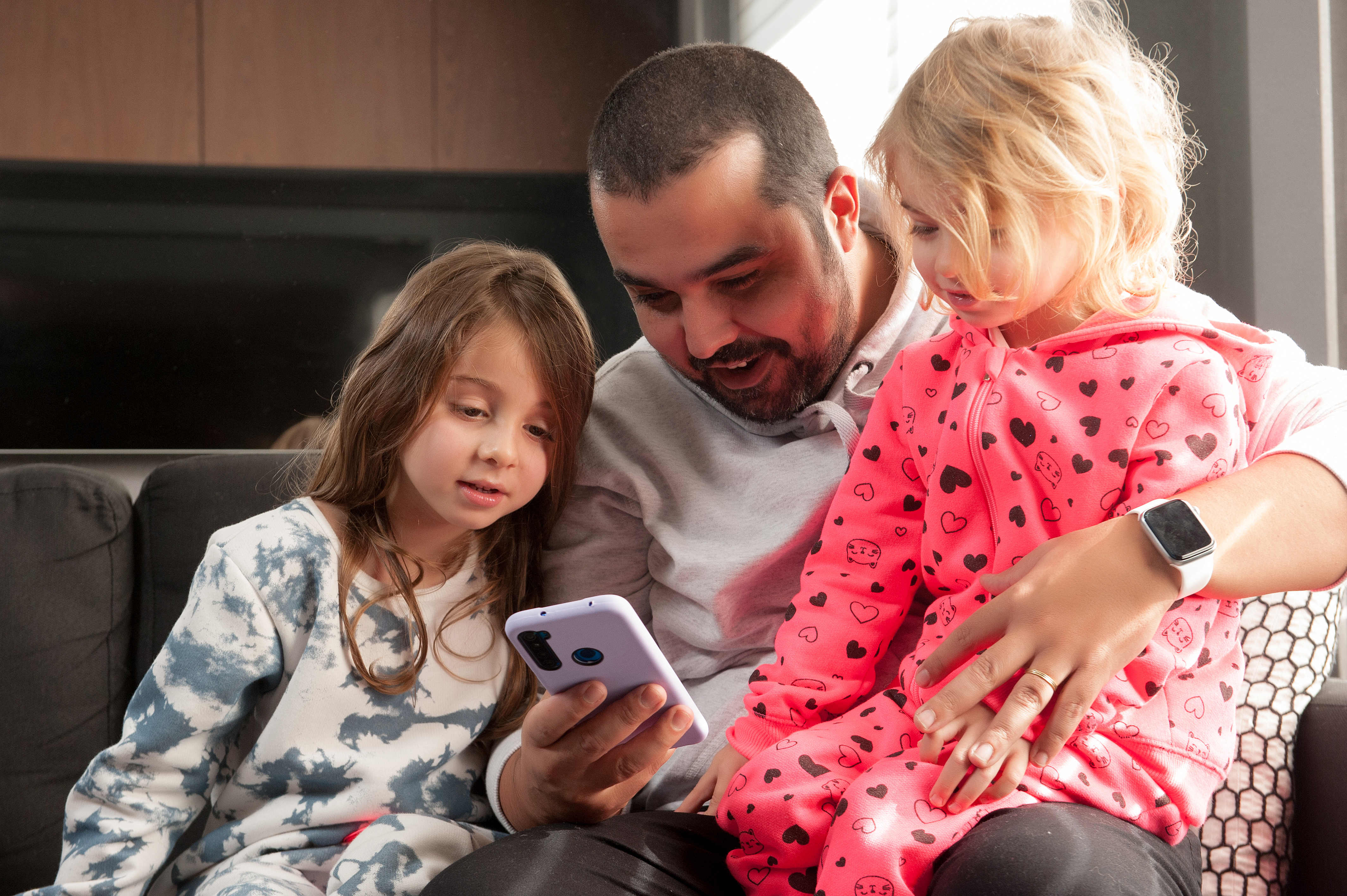 A foto mostra o pai com duas filhas pequenas mexendo no celular