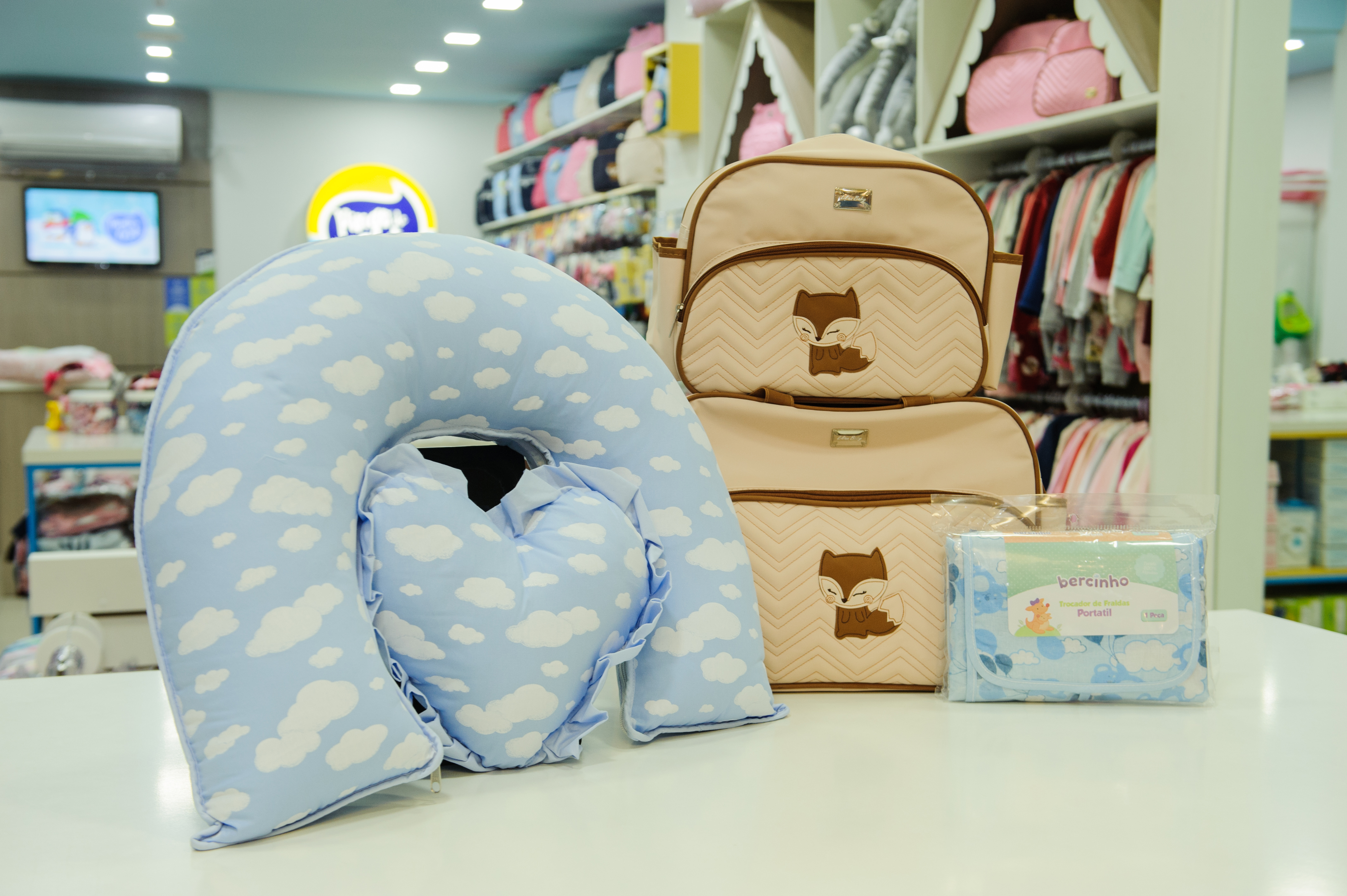 A foto mostra um travesseiro para amamentação, bolsa para maternidade e trocador de fraldas portátil.