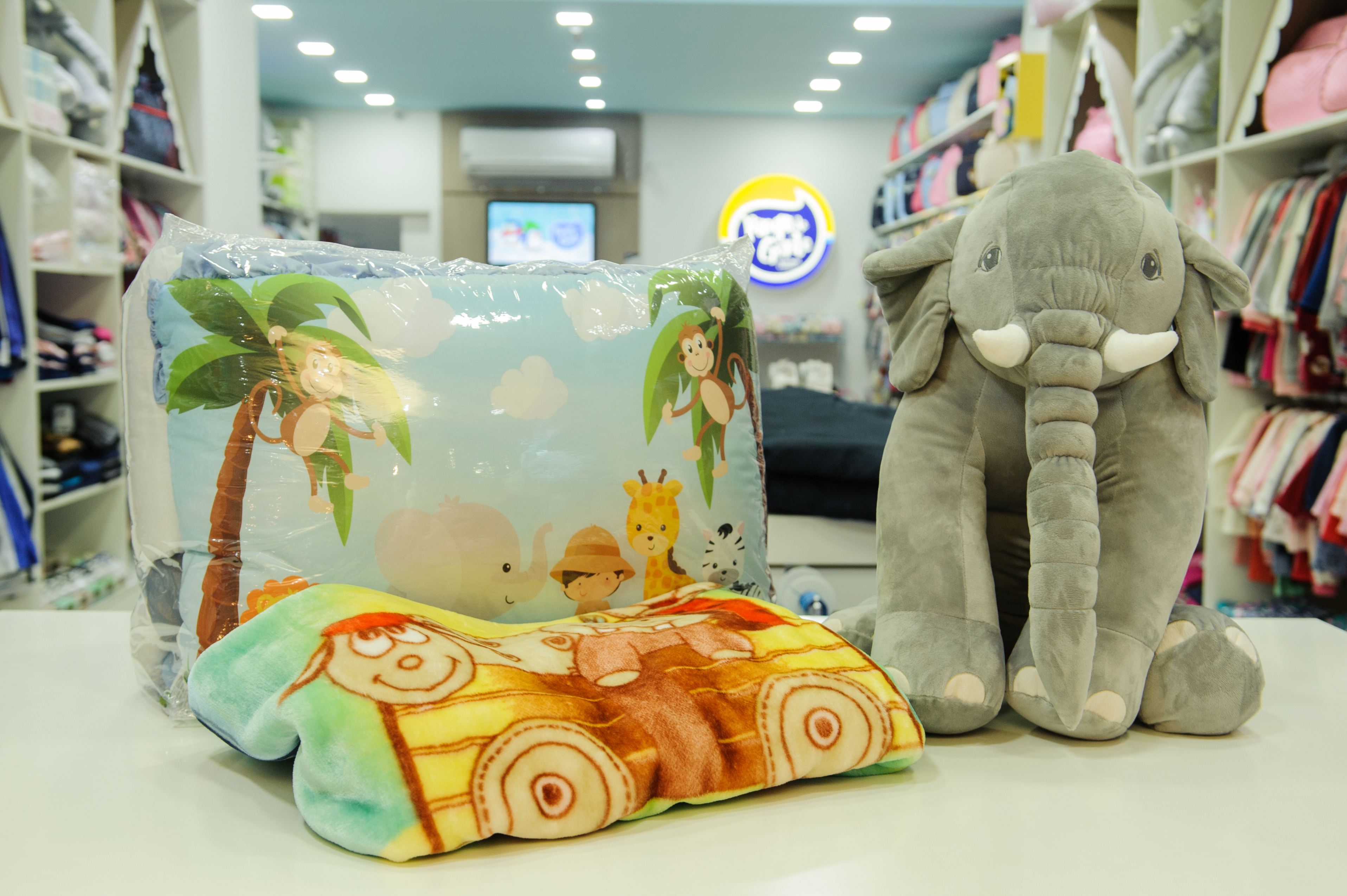 A foto mostra um conjunto de cama com desenho de animais e um elefante de pelúcia ao lado.